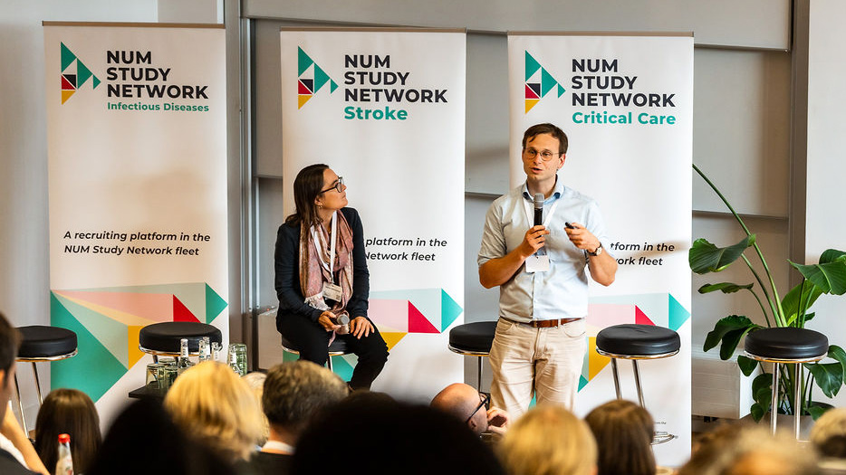 A speaker is speaking into a microphone on a stage at the NUM Study Network